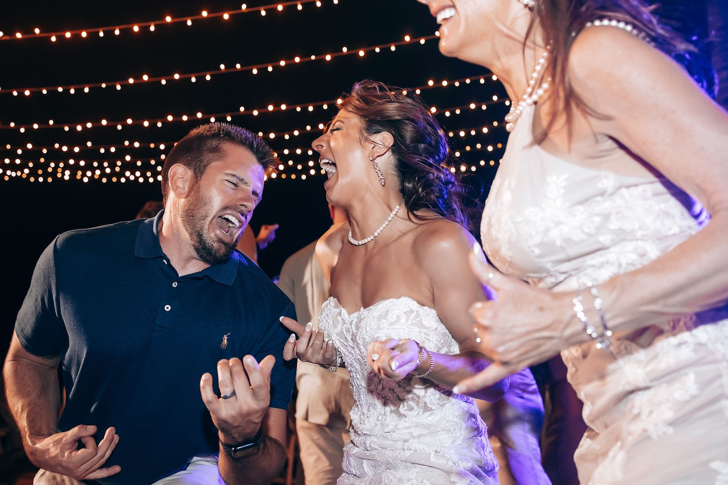 Joyful moments captured during evening wedding reception under string light decor.