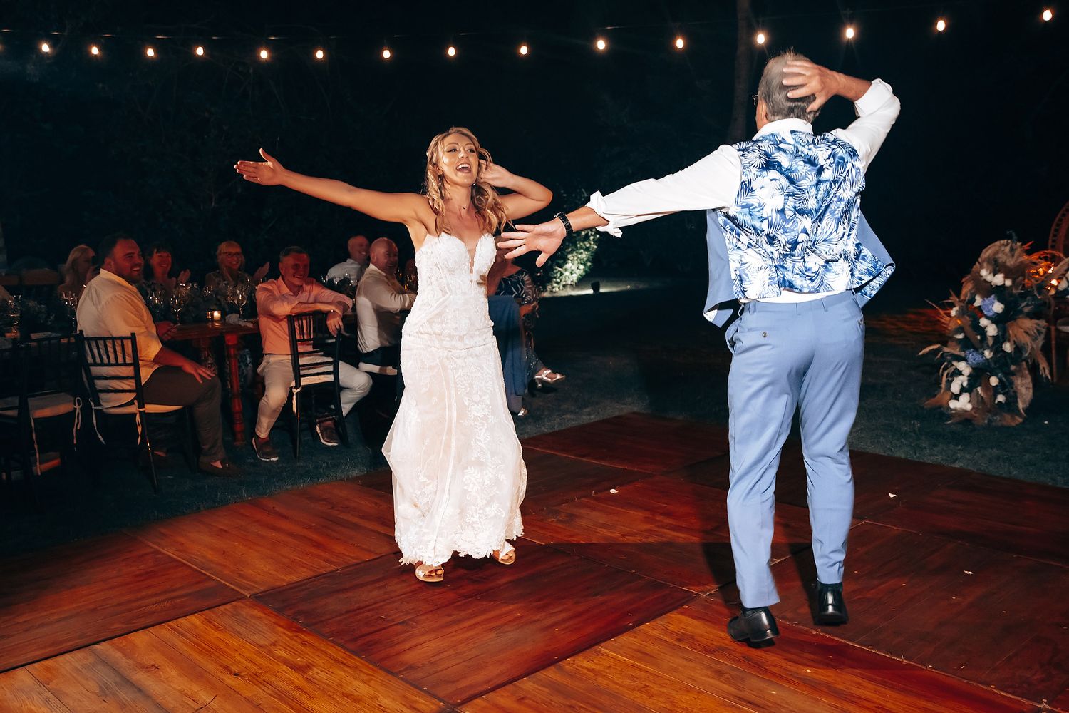 Wedding reception dance party with string lights overhead and guests dancing on wooden floor.