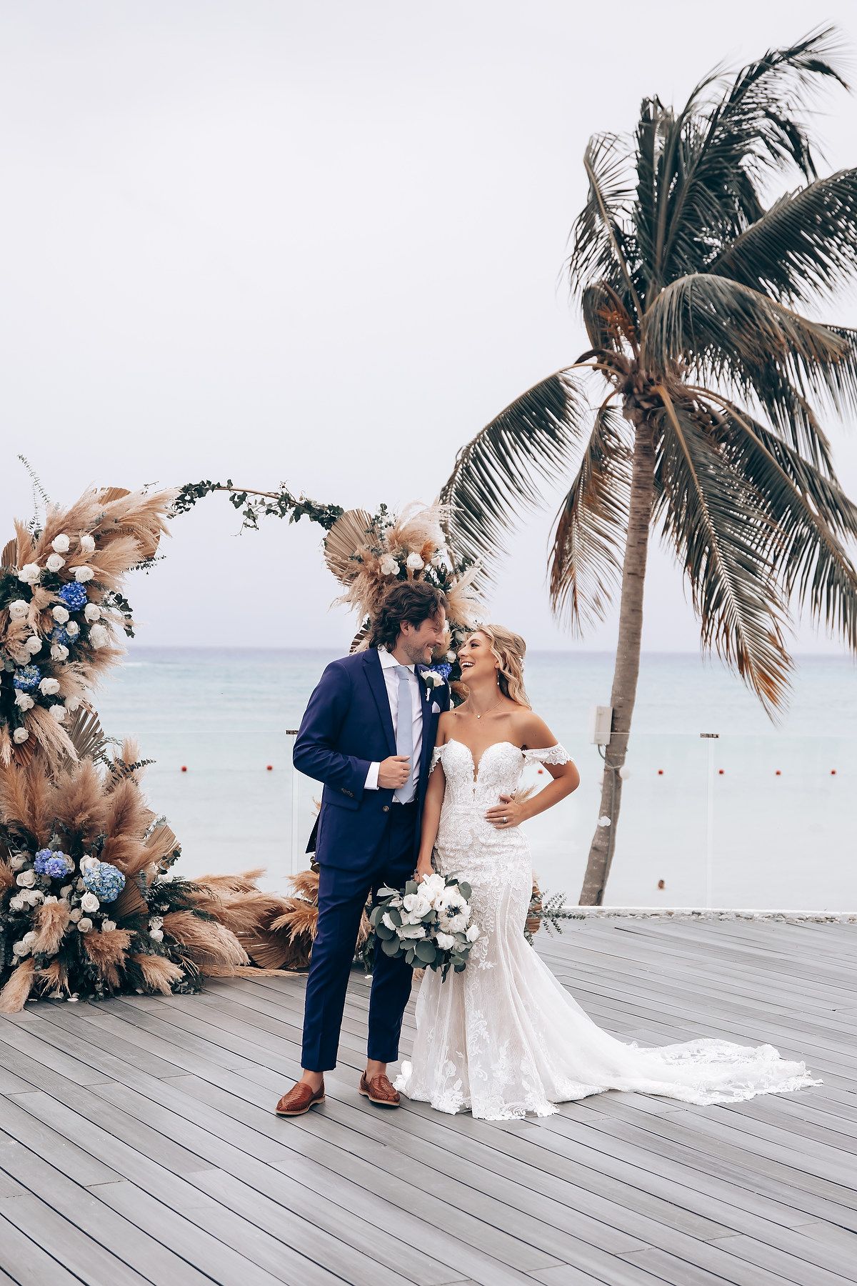 A romantic beach wedding ceremony with palm trees and ocean views on a wooden deck.