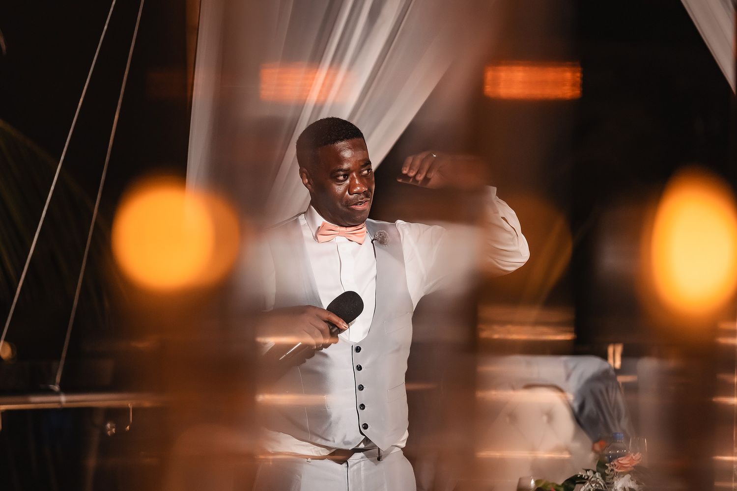 Performer in white suit sings passionately on stage with warm lighting and bokeh effects in the background.