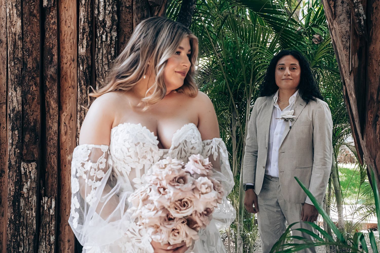 Wedding couple shares intimate moments against wooden walls with pink floral bouquet.