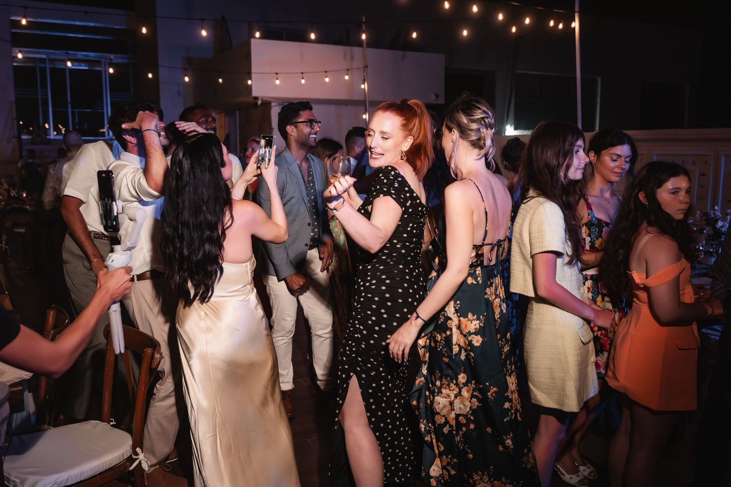 String lights illuminate wedding reception dance floor as guests celebrate.