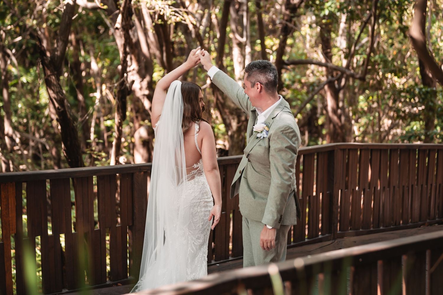Sunlight filters through trees onto a wooden walkway during an intimate wedding moment.
