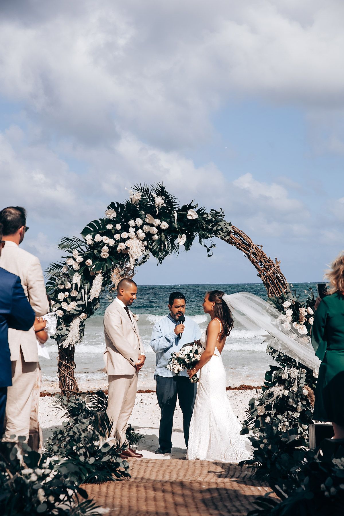 Beachfront wedding ceremony under floral arch with ocean waves in background.
