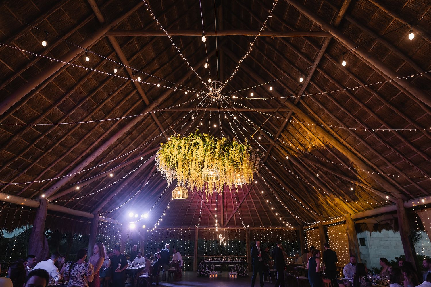 Rustic barn reception venue with twinkling string lights and high wooden beams.
