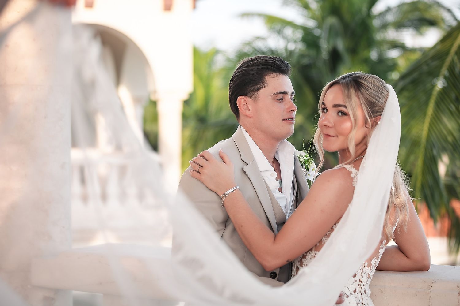 Romantic wedding couple shares intimate moments against a tropical palm tree backdrop during golden hour.