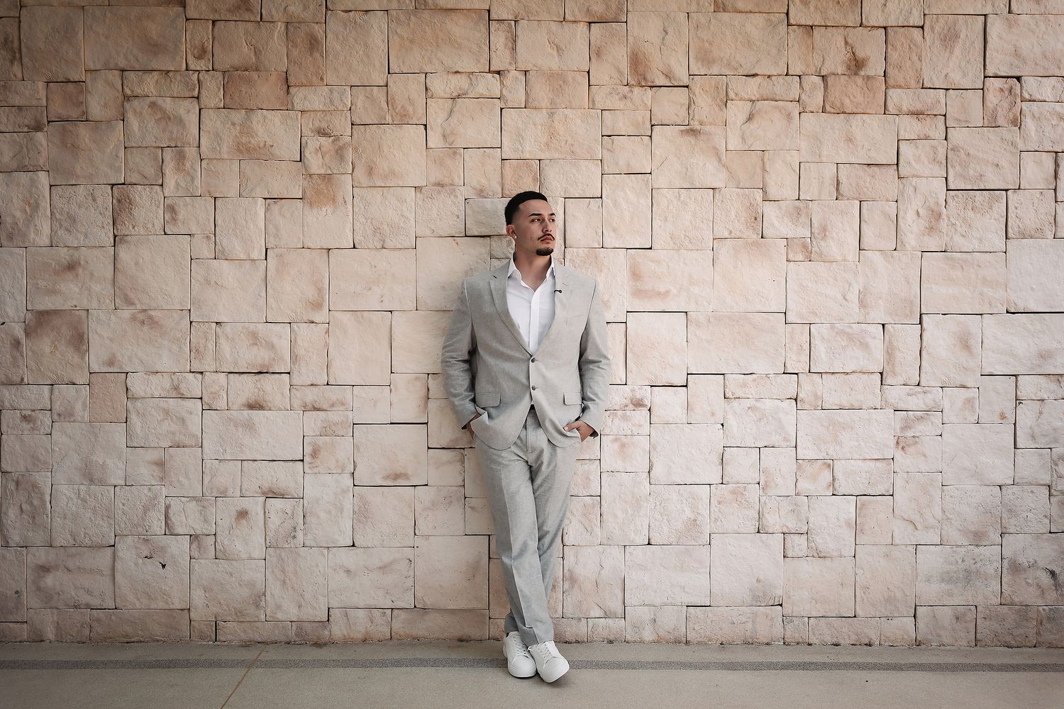Person in light colored formal wear standing against textured stone wall.