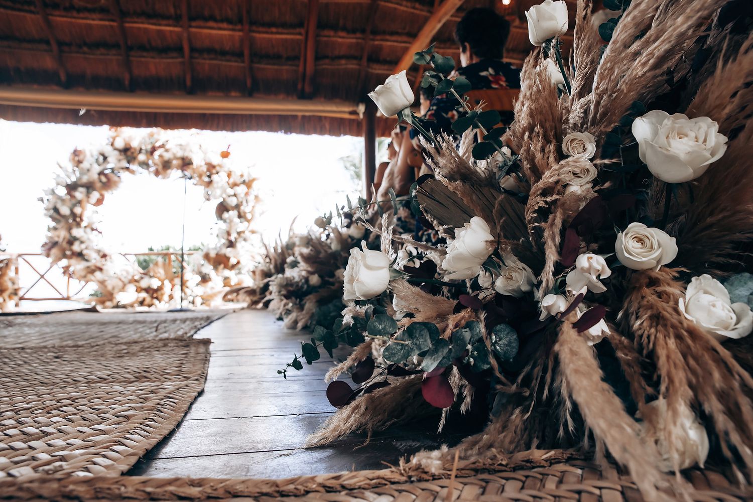 White roses and dried floral arrangements frame a beachfront wedding ceremony space.