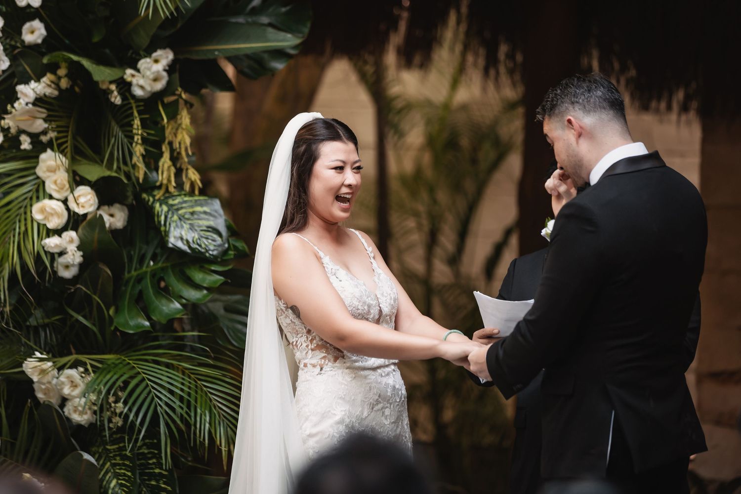 A romantic wedding ceremony moment captured in a tropical garden setting with white floral decorations.