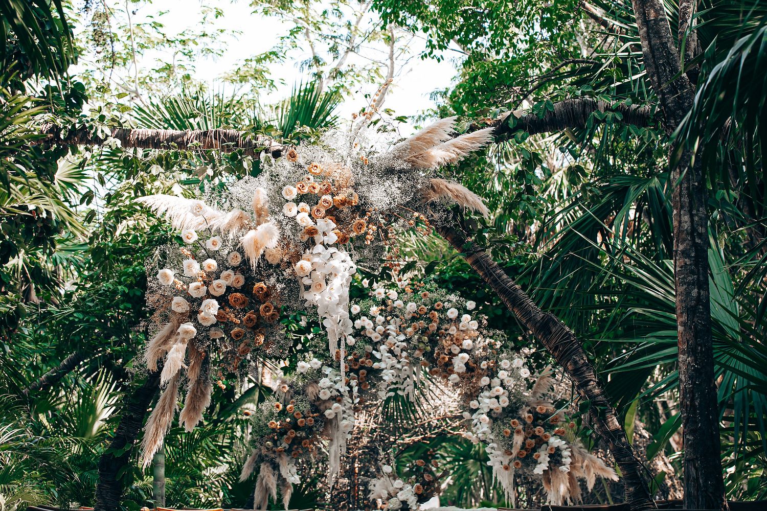 A row of dried palm fronds and flowers arranged in a natural boho style against a lush green tropical background.