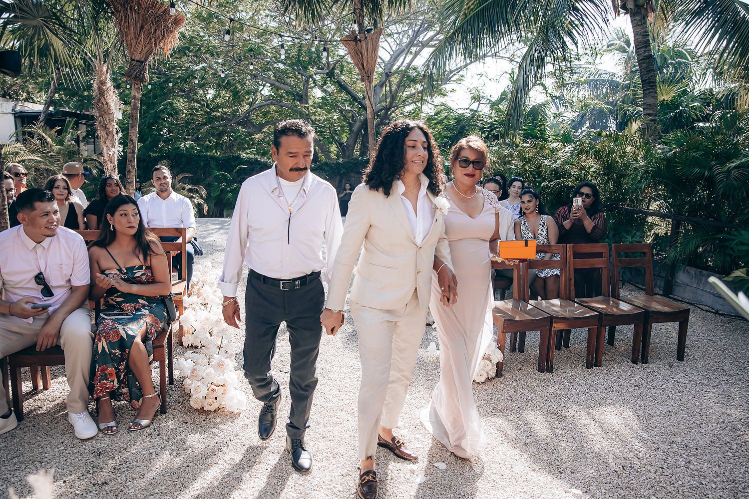 Wedding guests in white attire walking through a garden path during an outdoor celebration.