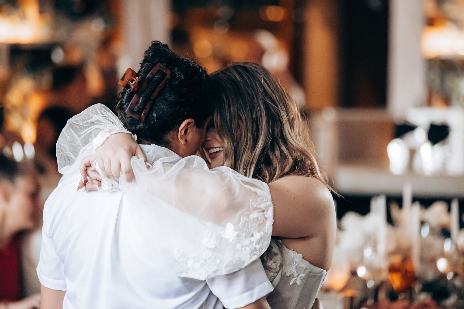 A couple shares a romantic dance at their wedding reception with warm lighting and guests in the background.
