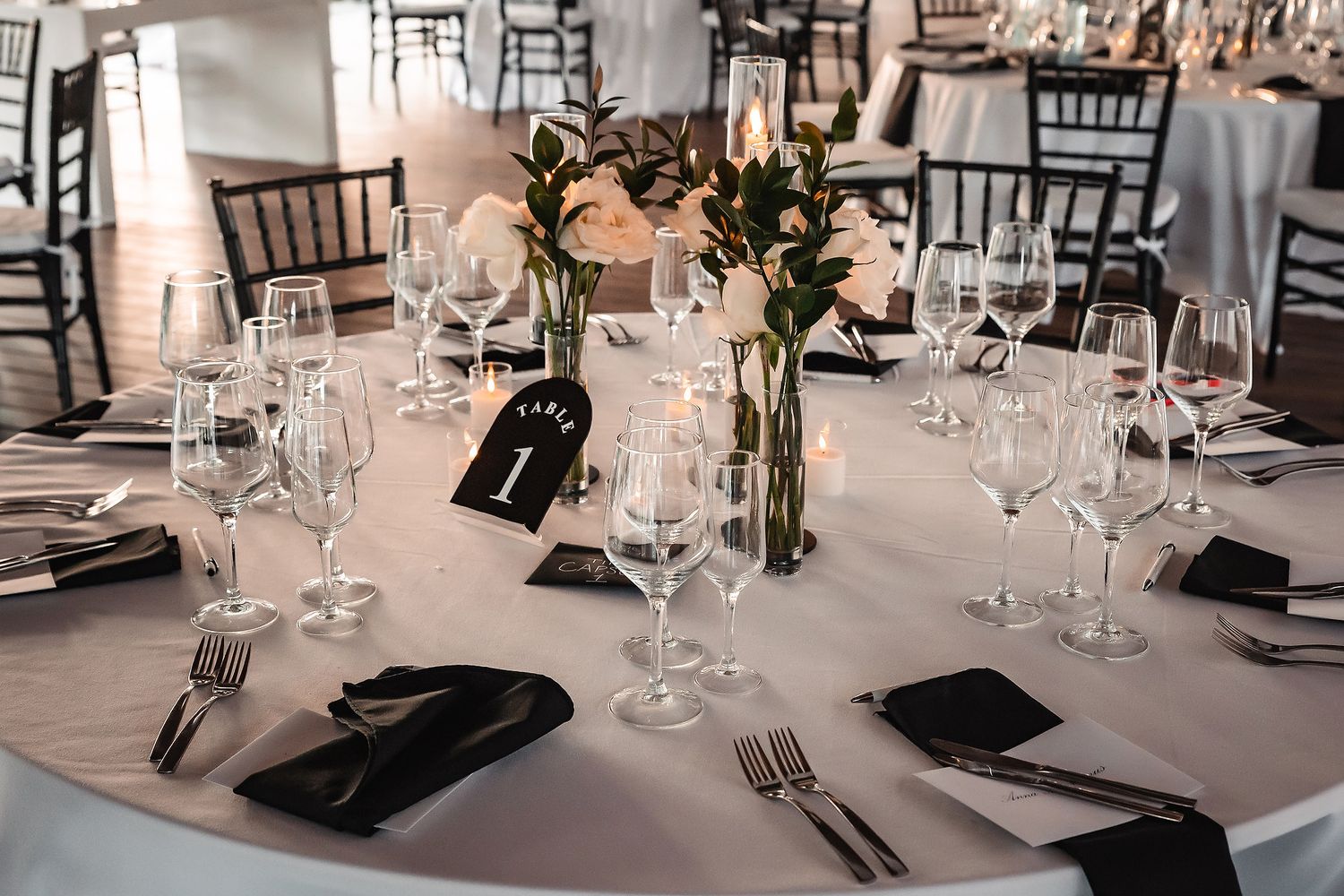 Formal table settings with black napkins, wine glasses, and centerpieces at a wedding reception.