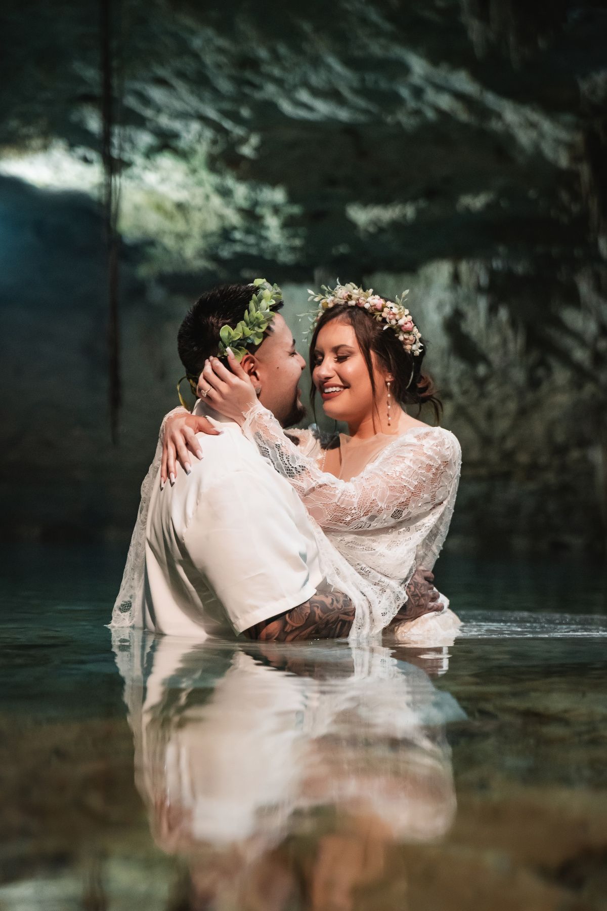 Couple in wedding attire sharing romantic moment in turquoise cenote waters.