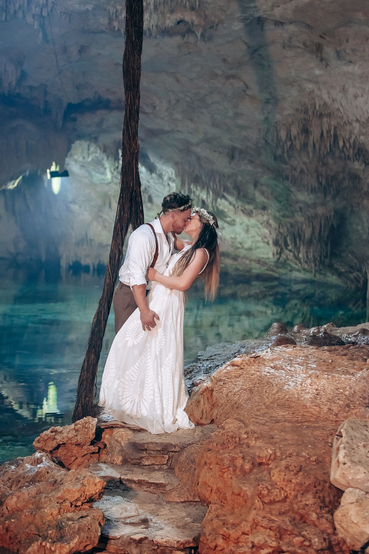 Romantic moment captured on rocky ledge inside illuminated cave setting.