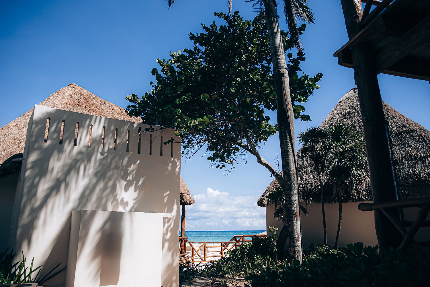 Panoramic view of white beach bungalows with thatched roofs against a bright blue tropical sky.
