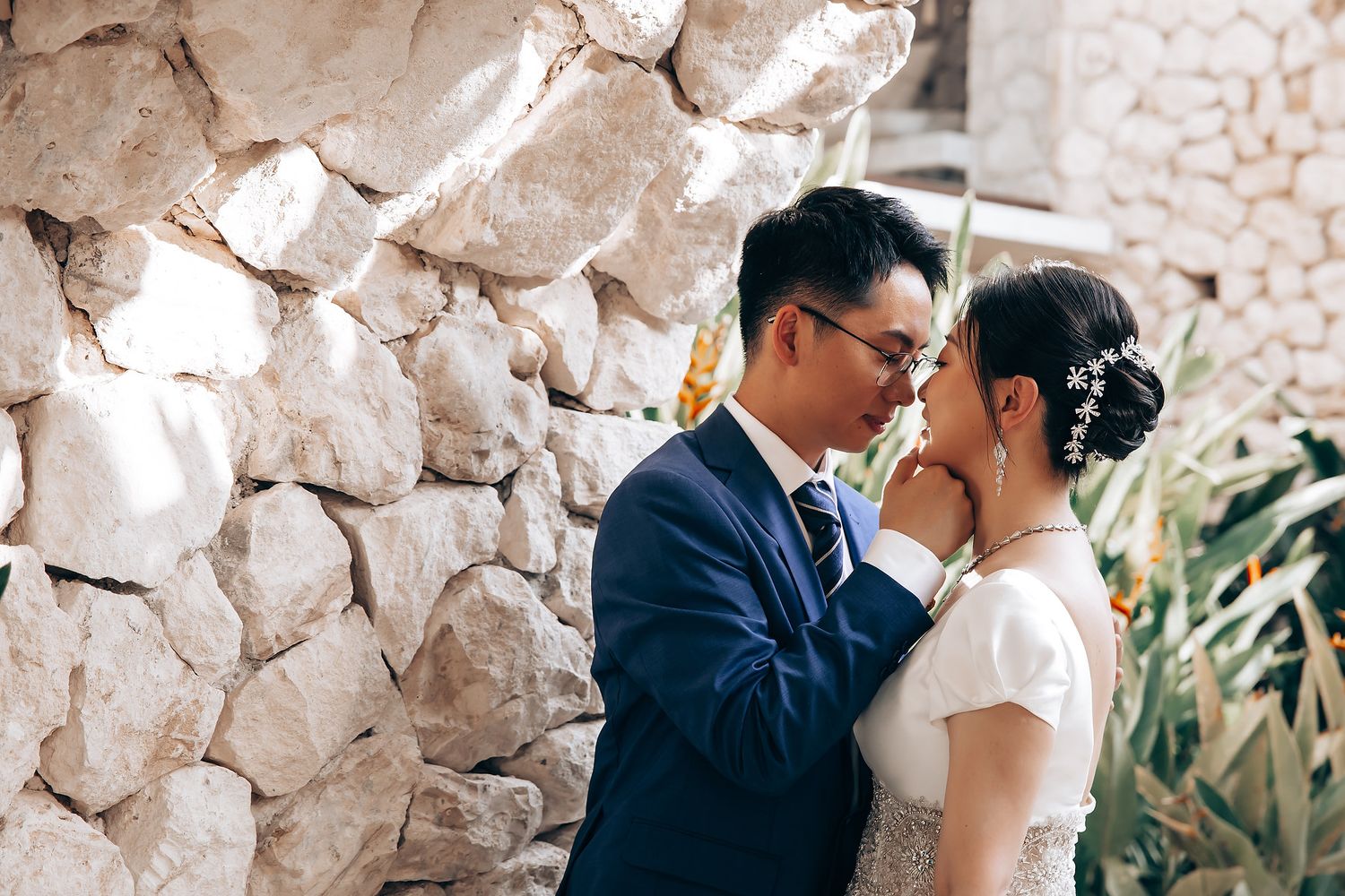 A couple shares an intimate moment against a rustic stone wall during their wedding celebration.
