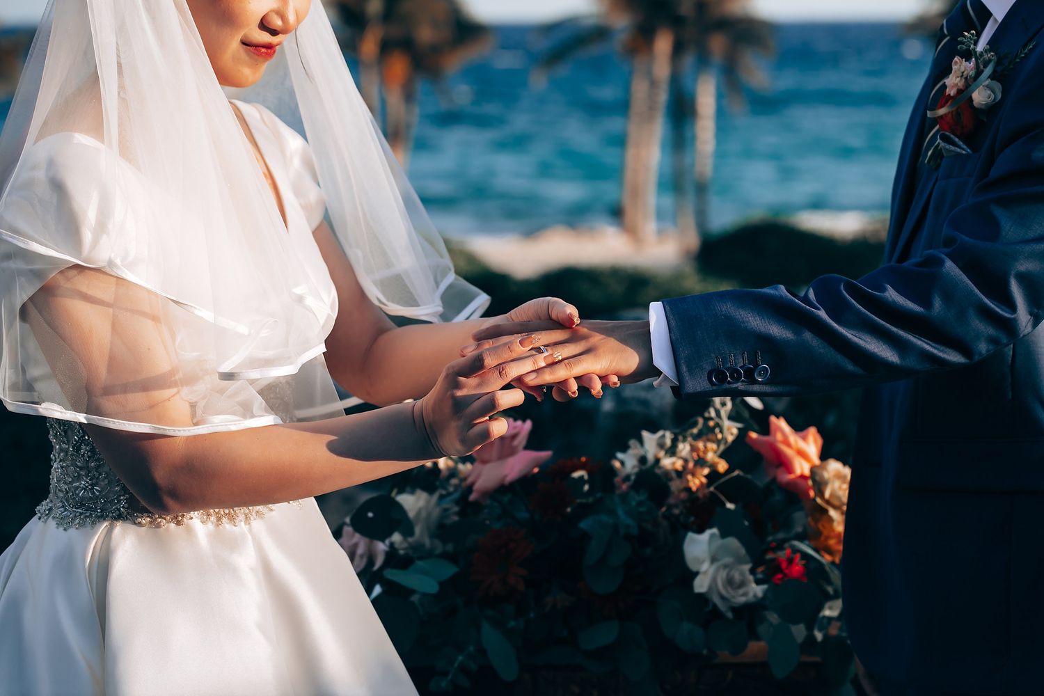 Intimate oceanside wedding ceremony with floral decorations and blue waters in background.