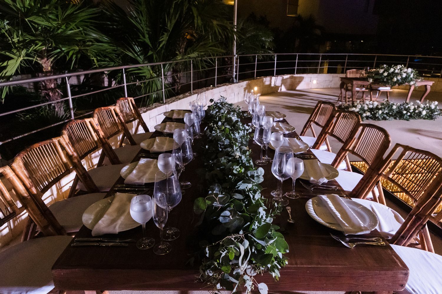 Elegant outdoor dinner table set with glassware and greenery garland centerpiece on a yacht deck at night.