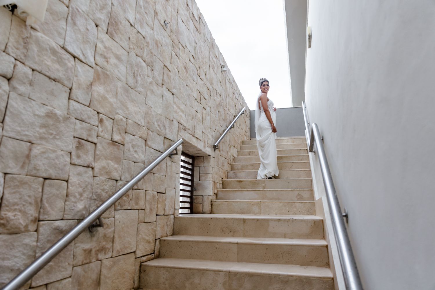 Elegant bride walking down outdoor stone stairs with metal railings at a luxury venue.
