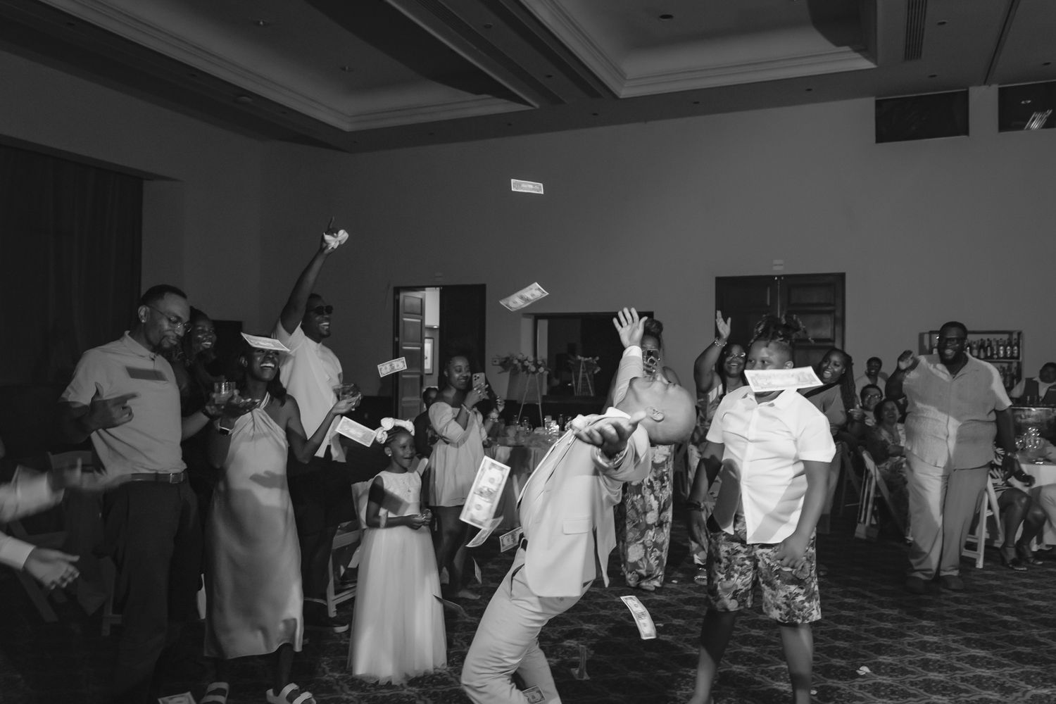 Black and white photo of wedding guests dancing and celebrating joyfully in a banquet hall reception.