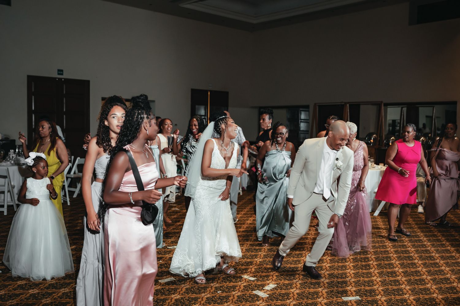 Wedding reception dance floor with bride, groom, and guests celebrating in elegant attire at a ballroom venue.