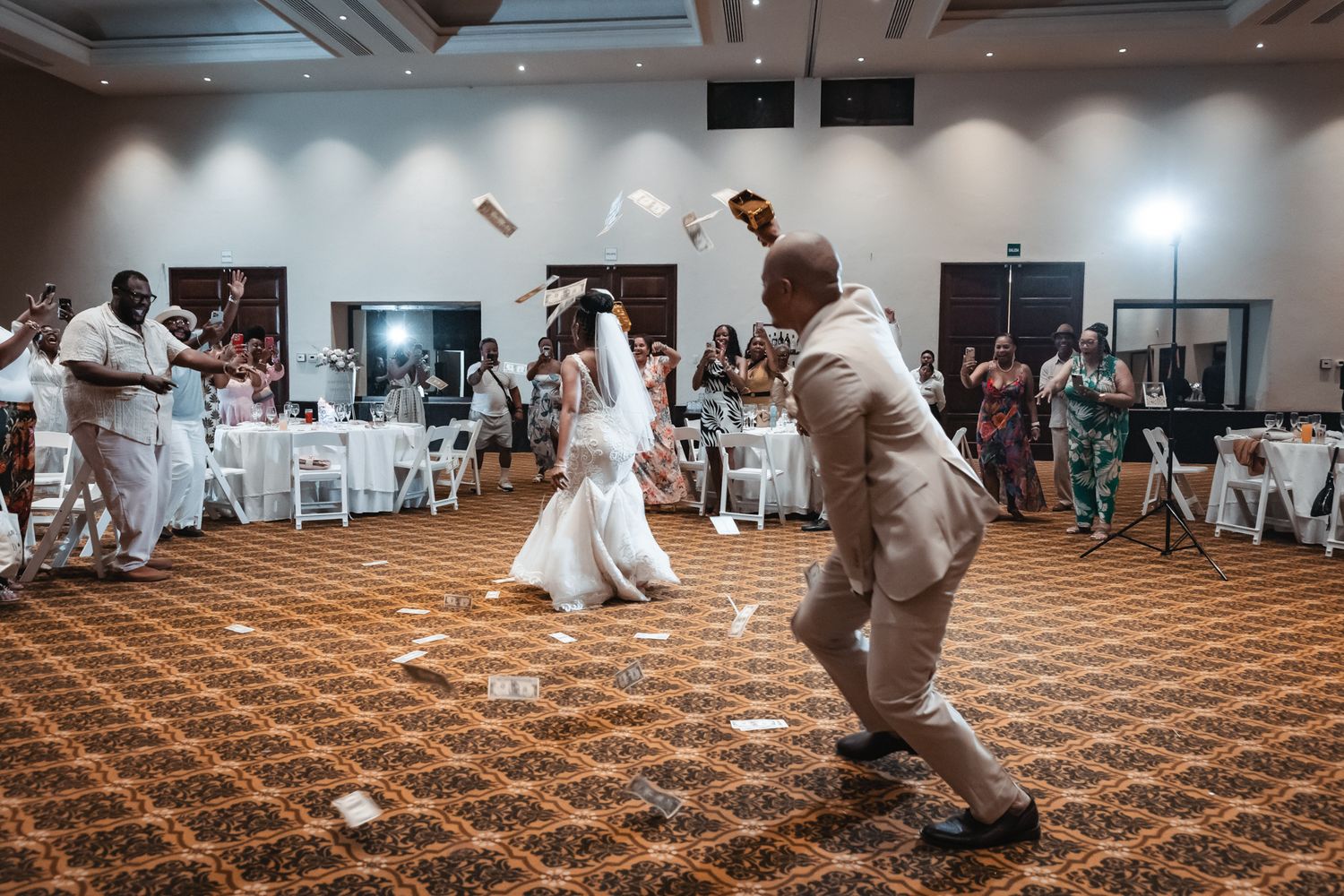 Bride and groom dancing joyfully as money is tossed in the air at their wedding reception.