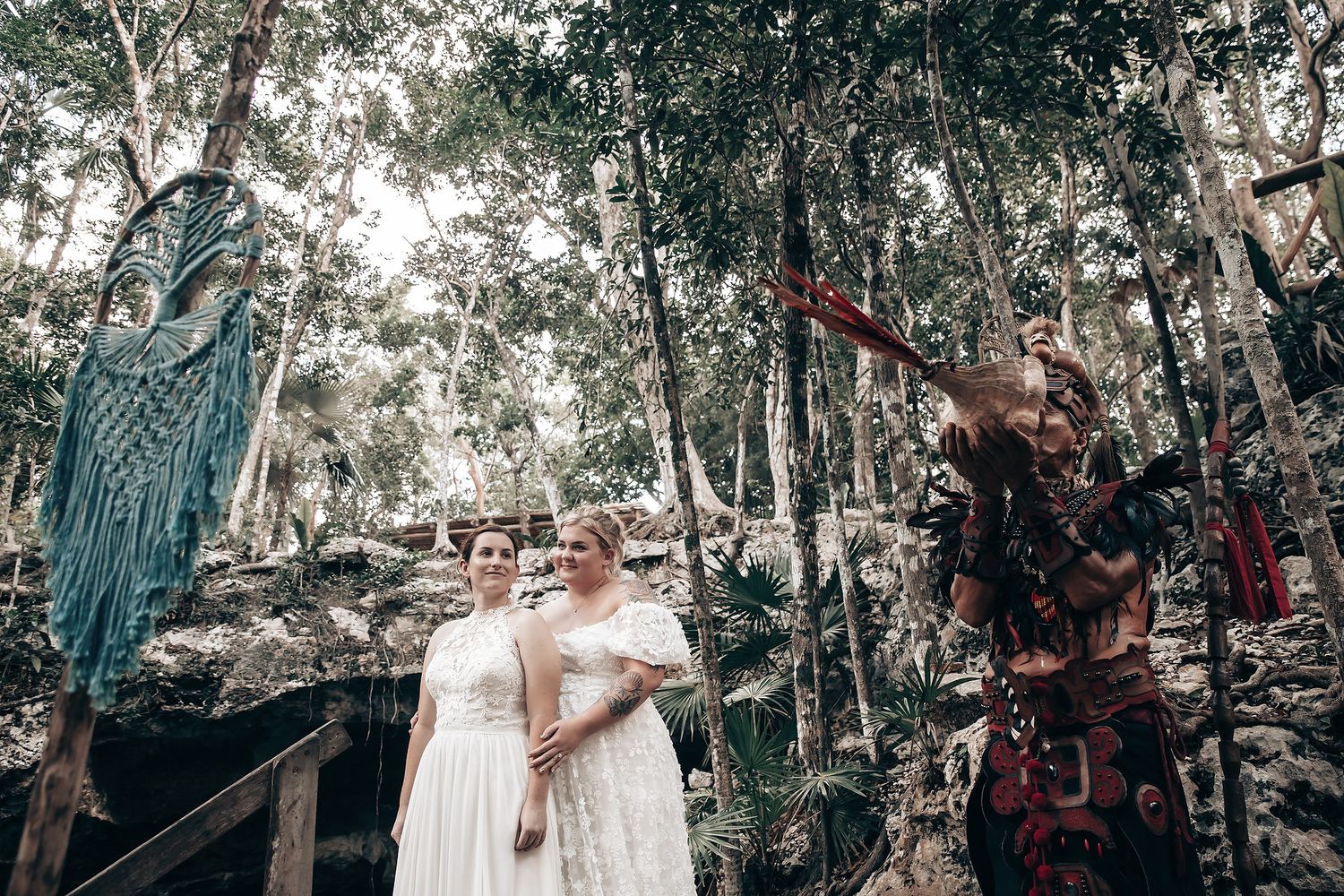 The image depicts a bride and groom standing in a forest setting, surrounded by greenery and natural elements.