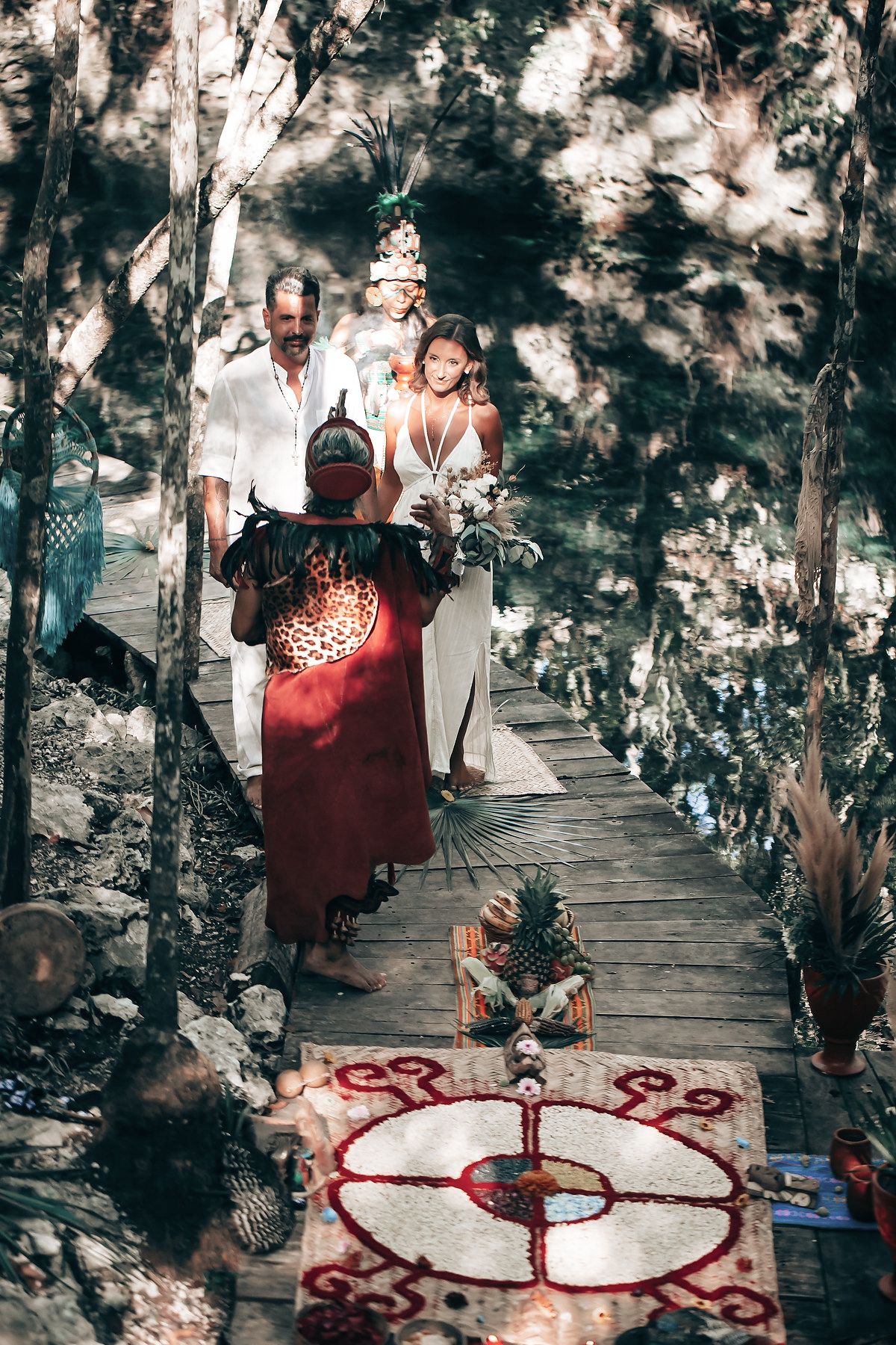 A couple walks along a wooden bridge in a lush, forested environment.