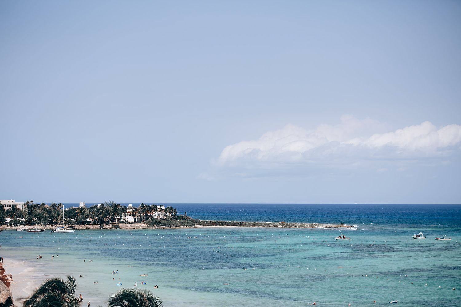 Aerial view of a tropical beach resort with turquoise waters and palm trees along the coastline.
