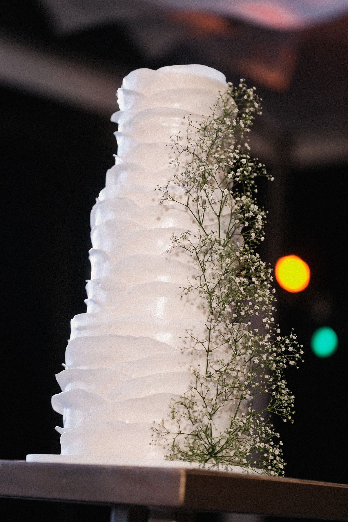 Elegant white tiered wedding cake decorated with ruffled fondant and delicate baby breath flowers.