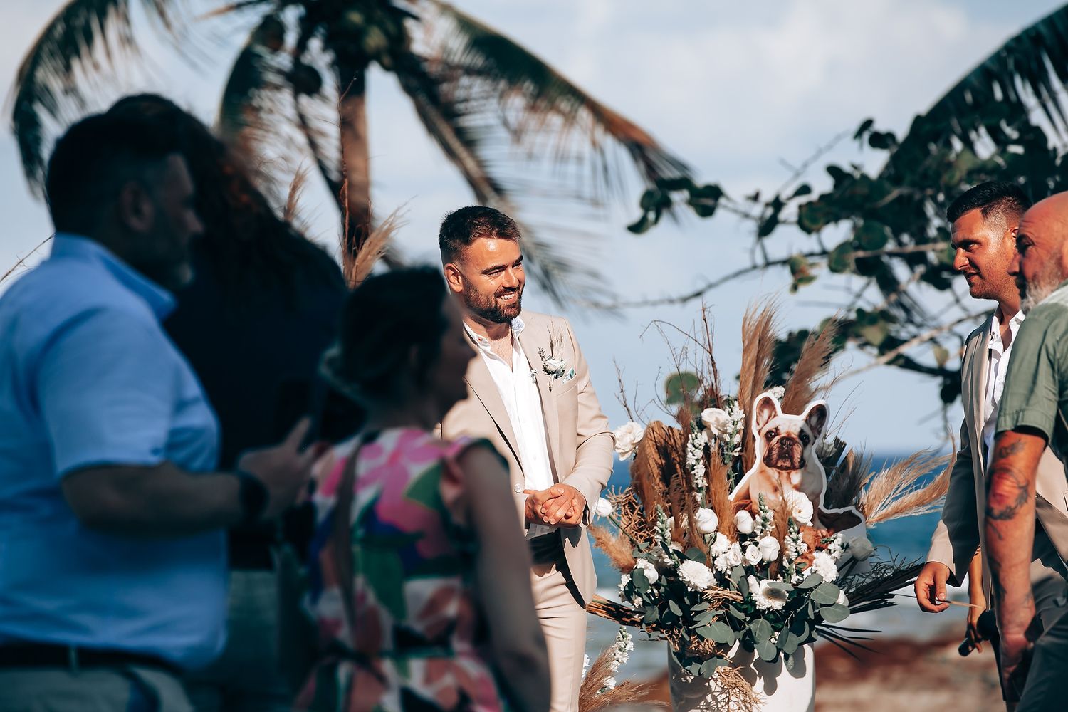Wedding ceremony guests seated outdoors with ocean views and tropical palm trees in the background.
