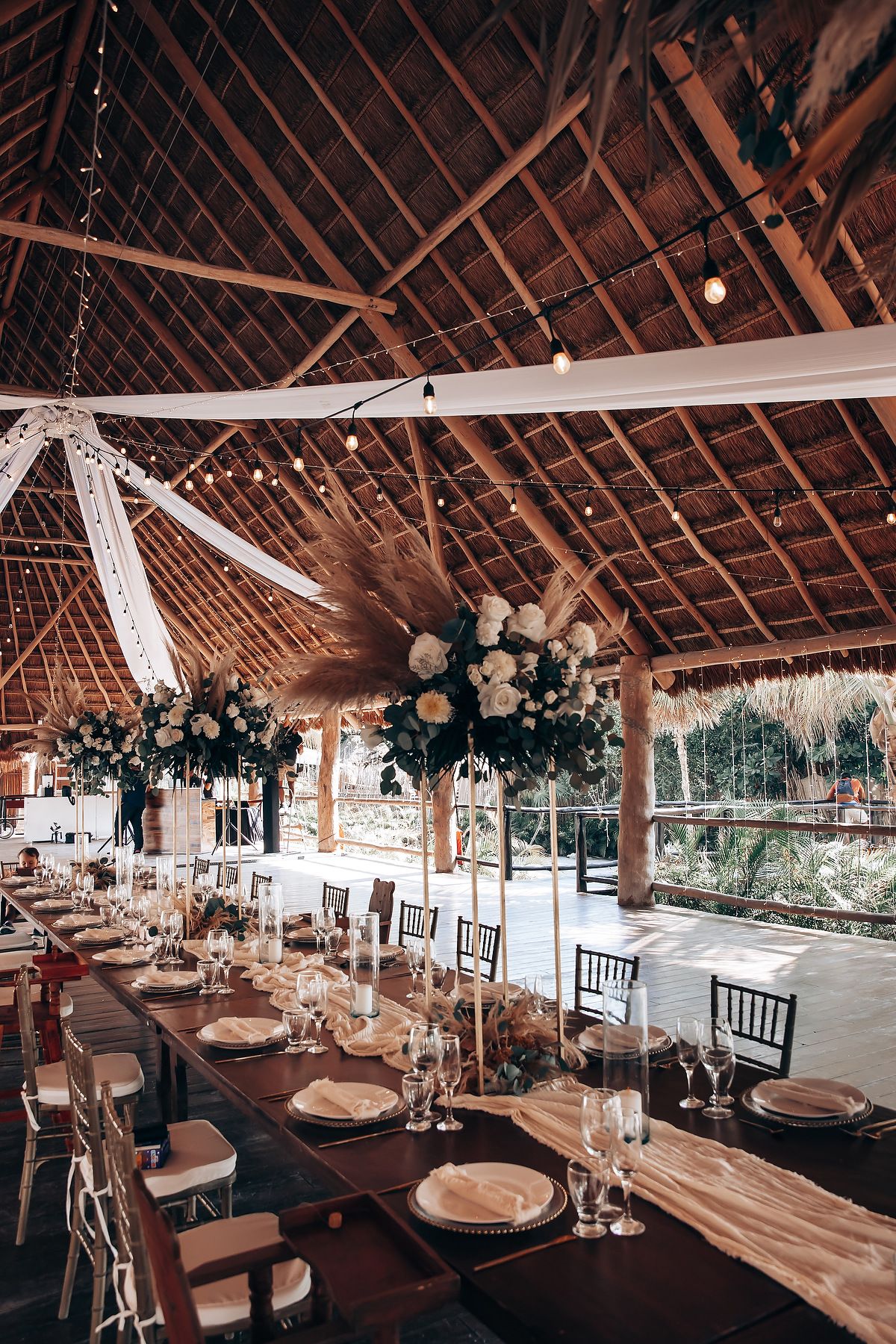 Rustic wooden reception venue with exposed beams and elegant table settings under hanging floral arrangements and chandeliers.