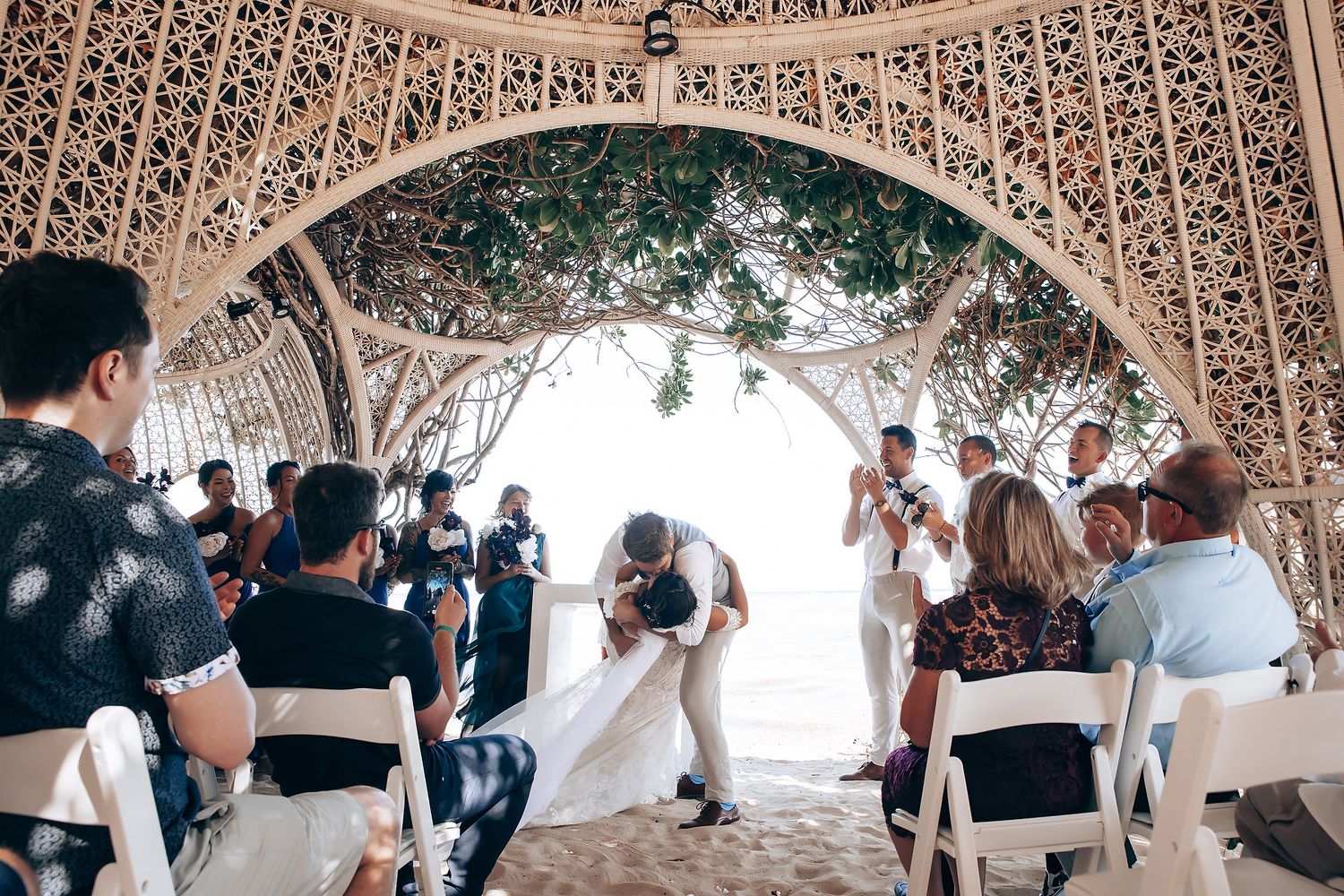 Wedding celebration under an intricate white latticed pavilion with natural greenery.