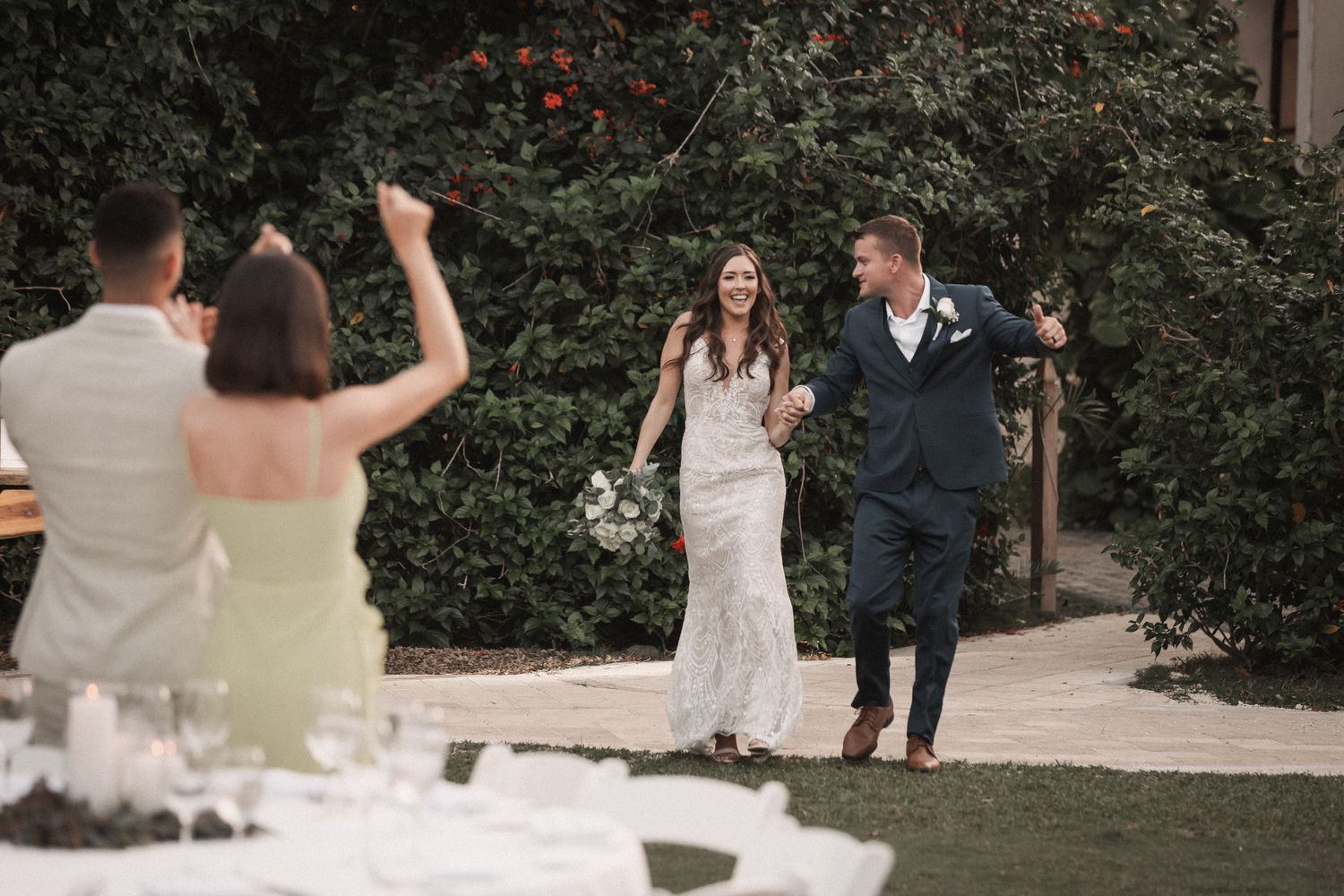 Joyful bride and groom make grand entrance to outdoor wedding reception greeted by cheering guests.