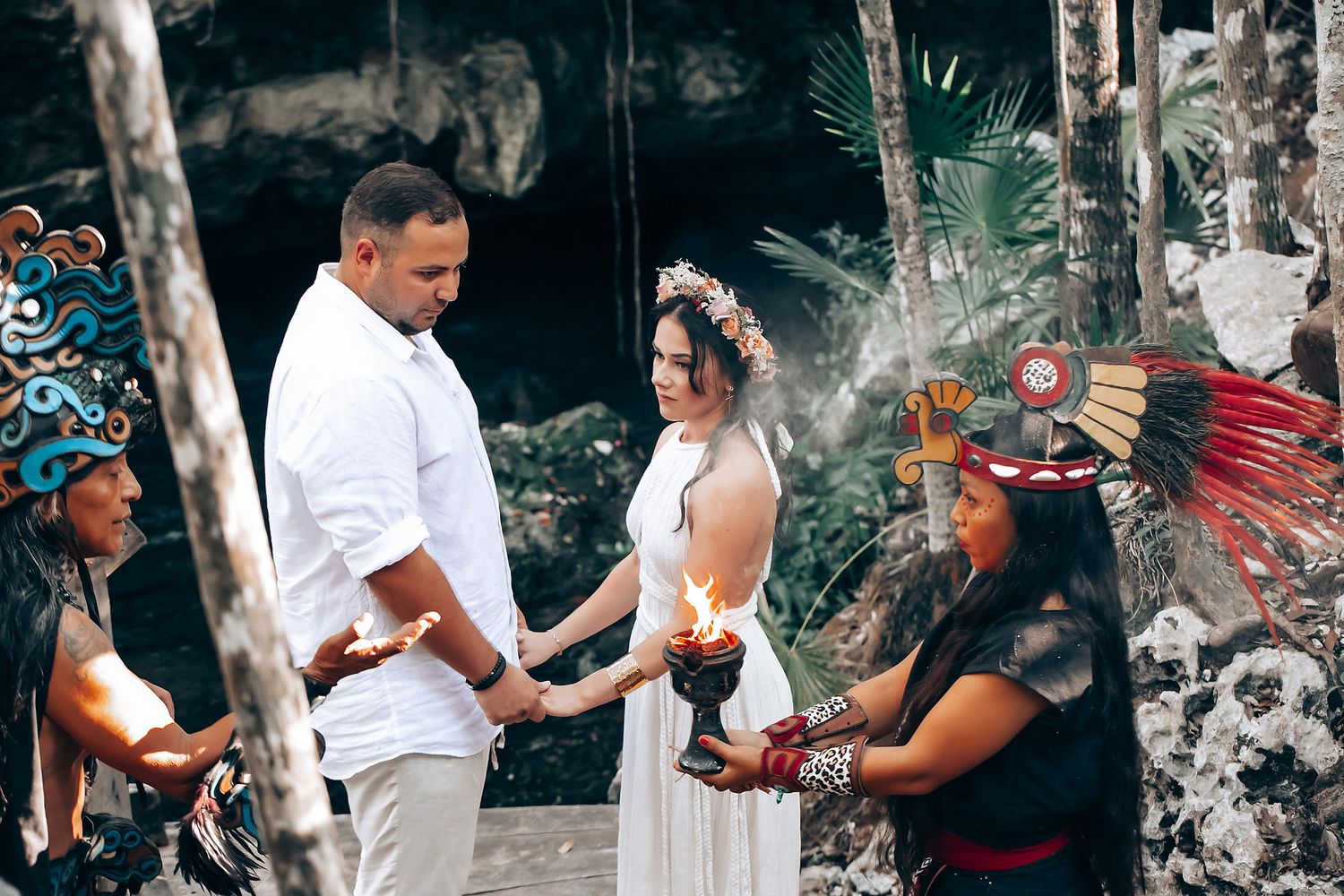 Outdoor ceremony scene with people gathered around blankets and traditional decorative elements.