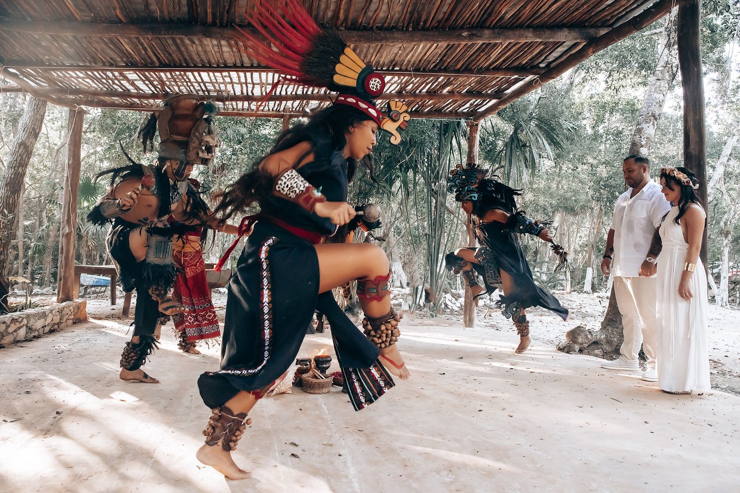 Participants perform traditional movements under a rustic wooden shelter.