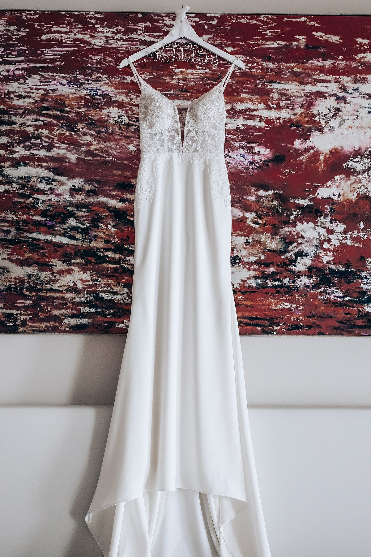 A white wedding dress hangs elegantly against a red and black abstract art backdrop.