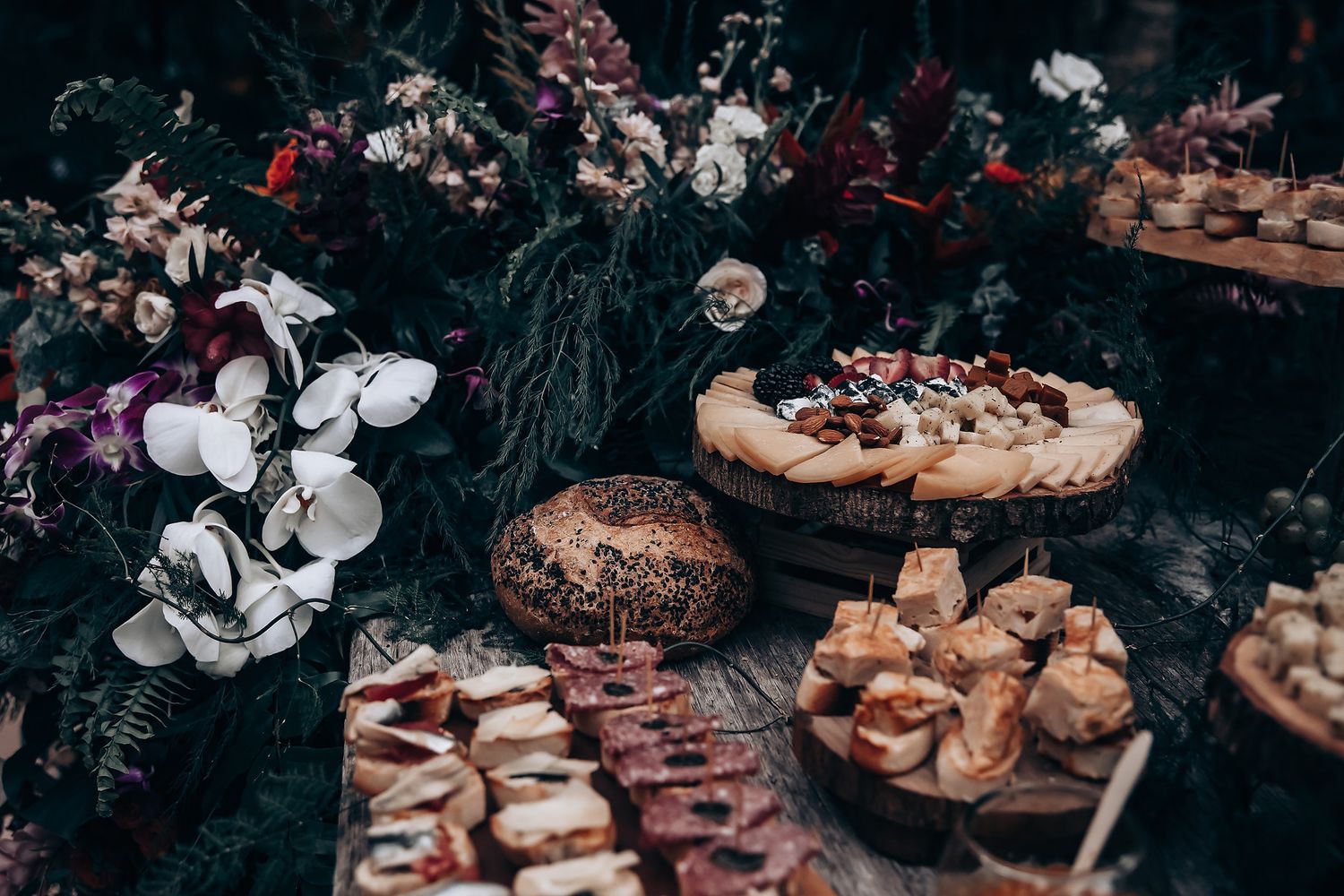 Rustic dessert table with assorted pastries, cakes, and floral decorations arranged on a dark wooden surface.