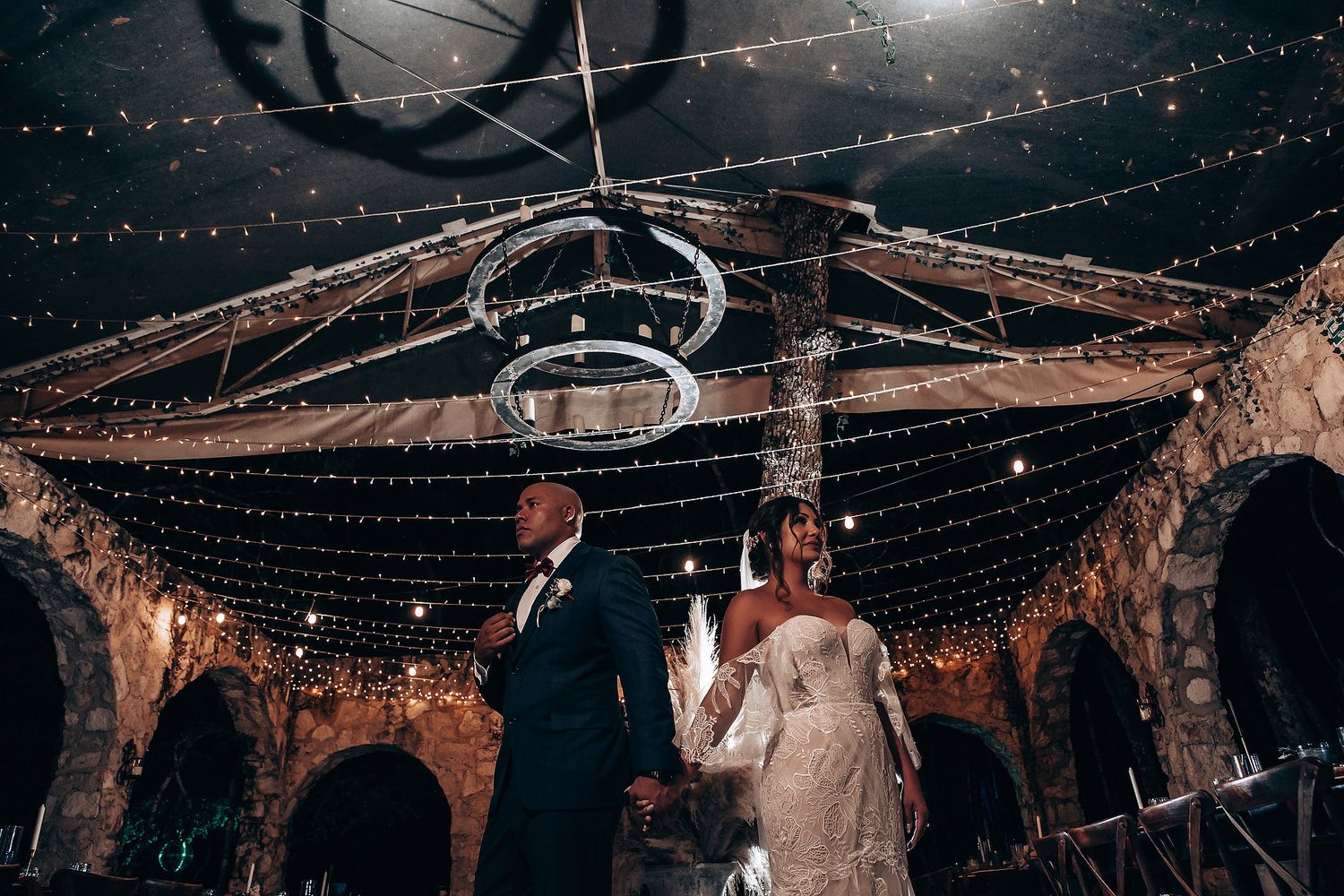 Couple dancing under canopy of twinkling lights in rustic stone venue.