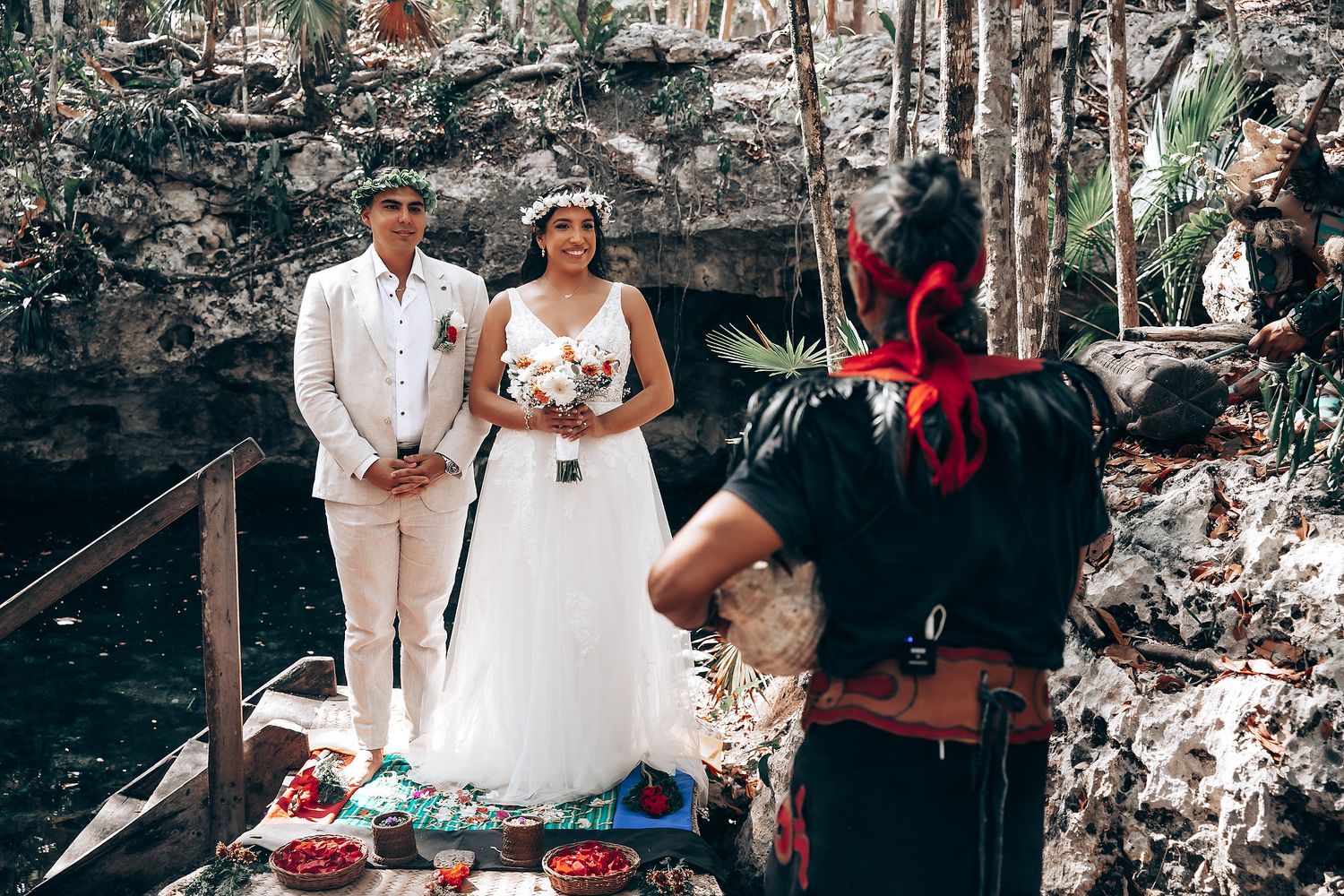 A couple in white wedding attire shares an intimate moment during an outdoor ceremony.