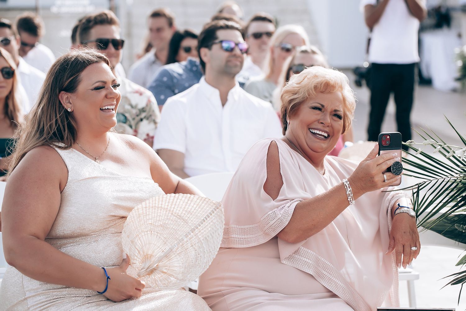 Wedding guests in light colored attire enjoying celebrations on an outdoor terrace.