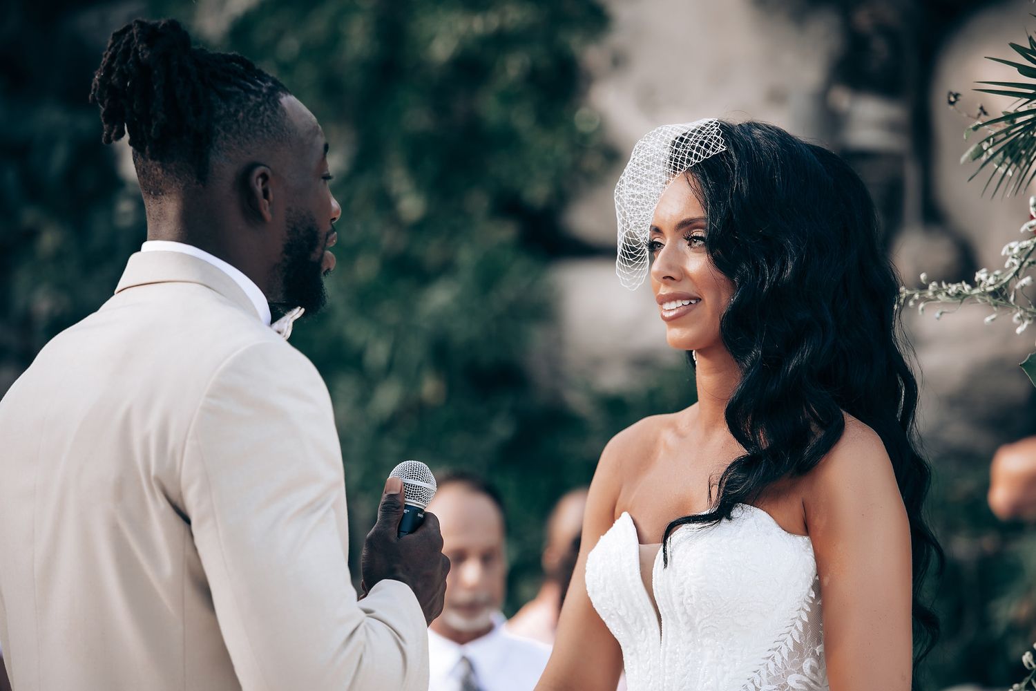 Elegant beach wedding ceremony with couple exchanging vows under tropical foliage.