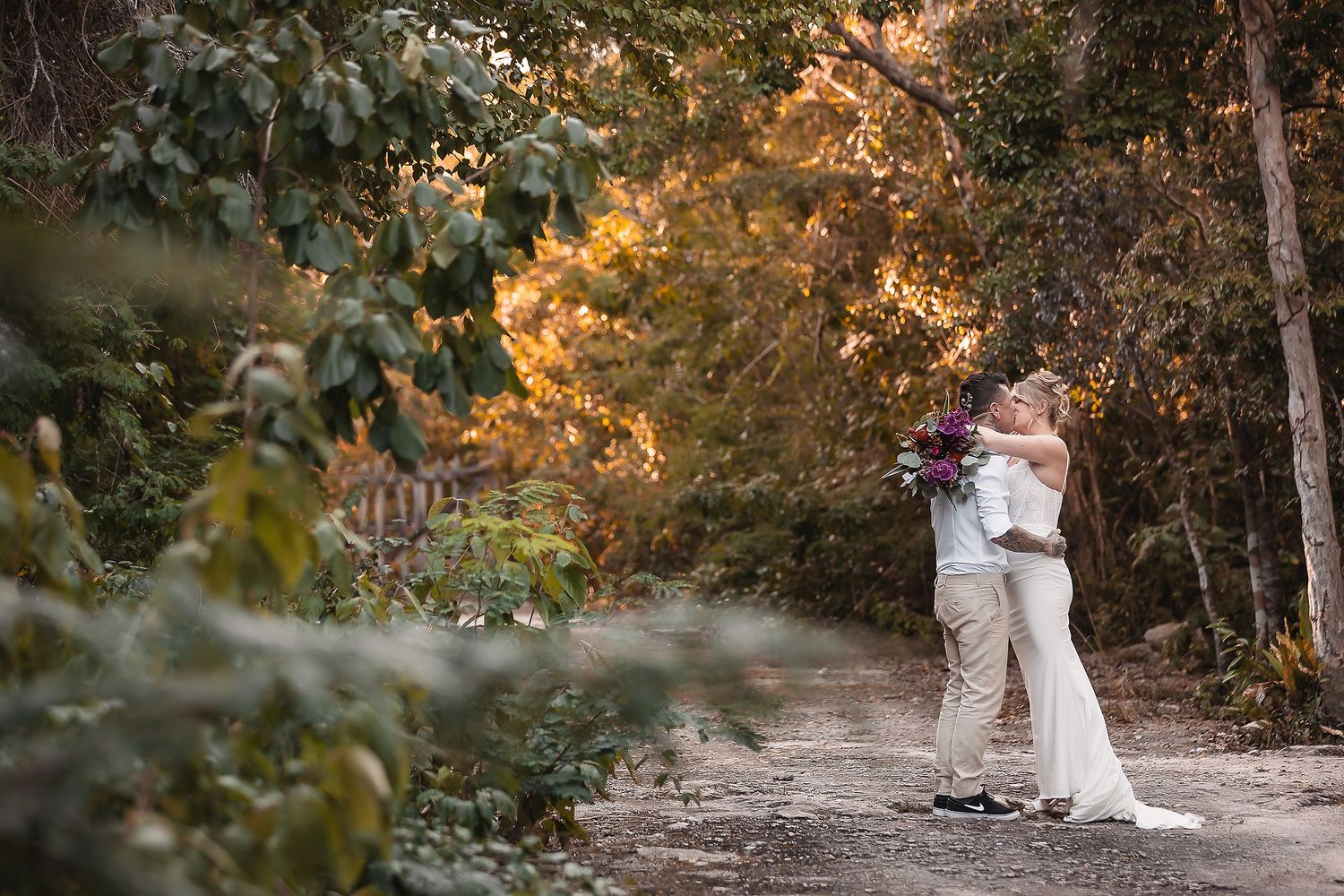 Bride and groom embracing on a forest path surrounded by autumn foliage during their outdoor wedding ceremony.