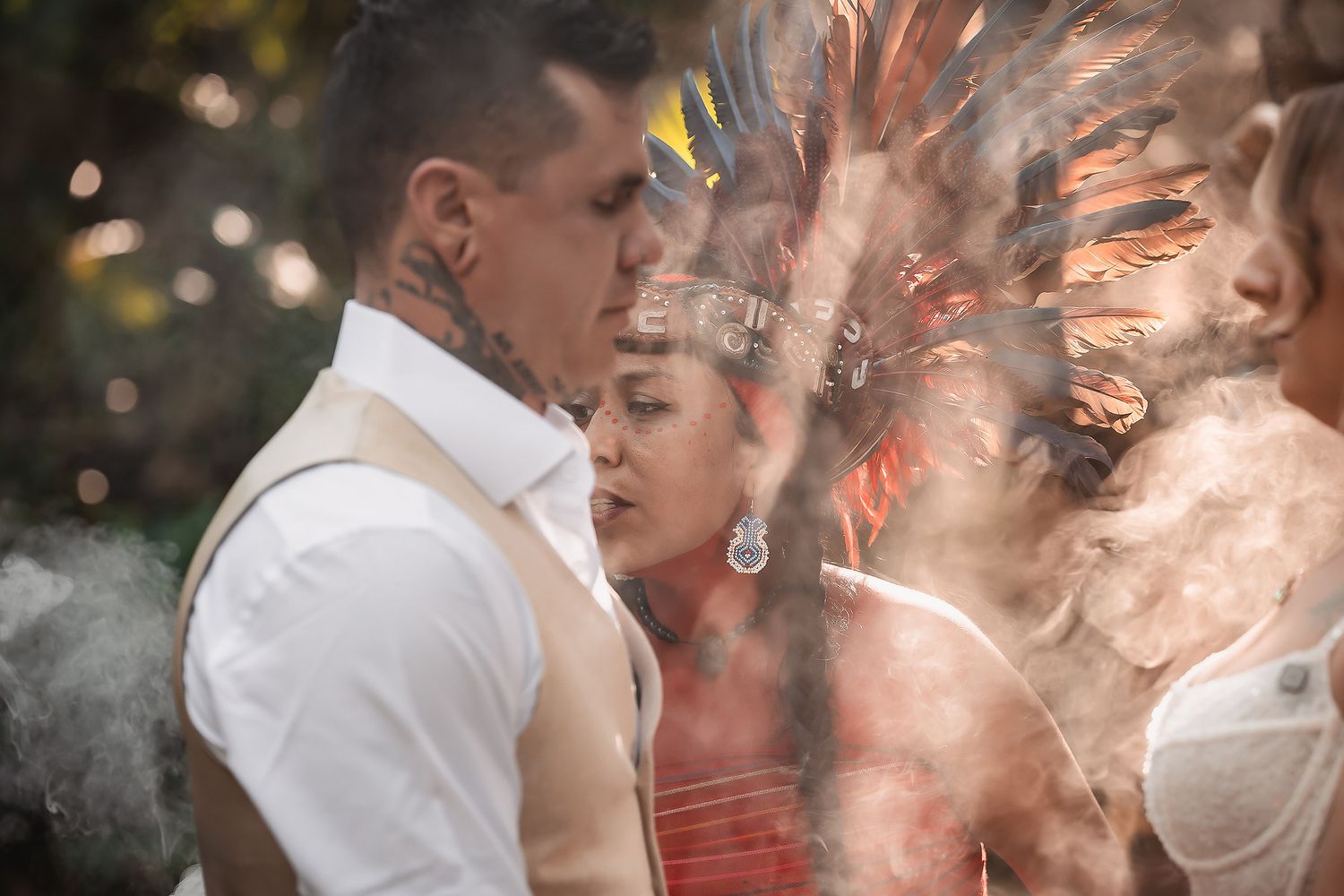 Couple in intimate embrace, man with tattoos and woman wearing Native American headdress, surrounded by smoke.