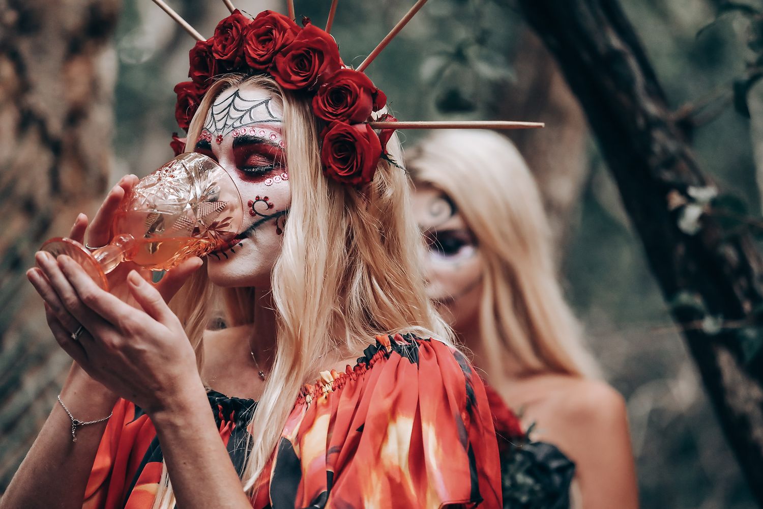 Dramatic Day of the Dead themed photoshoot featuring red roses and sugar skull makeup in a forest setting.