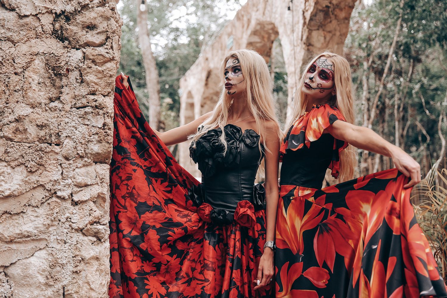 Women in flowing red and black dresses pose together in an outdoor woodland setting.
