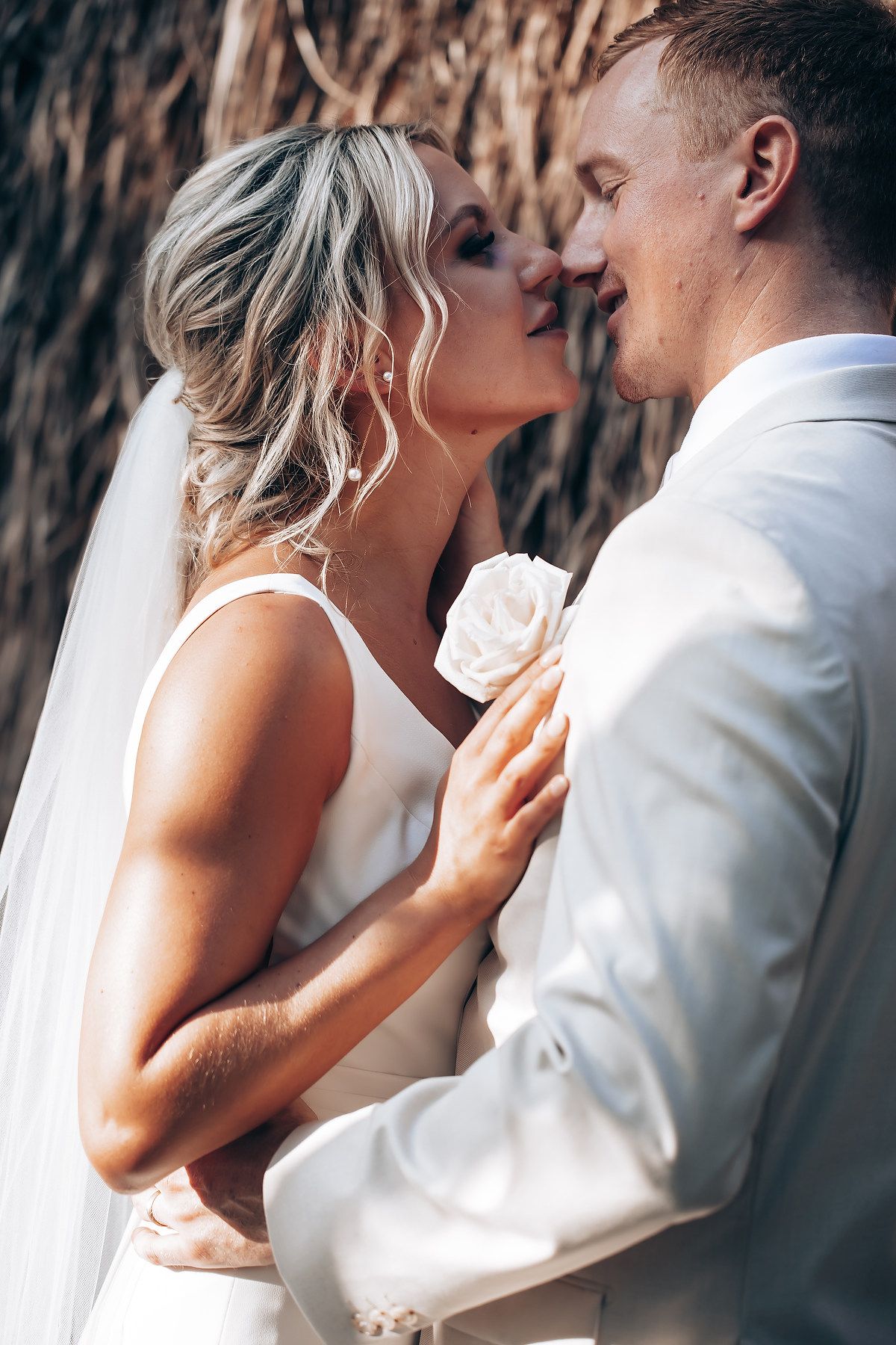 Romantic wedding couple shares intimate moments in white attire against rustic backdrop.