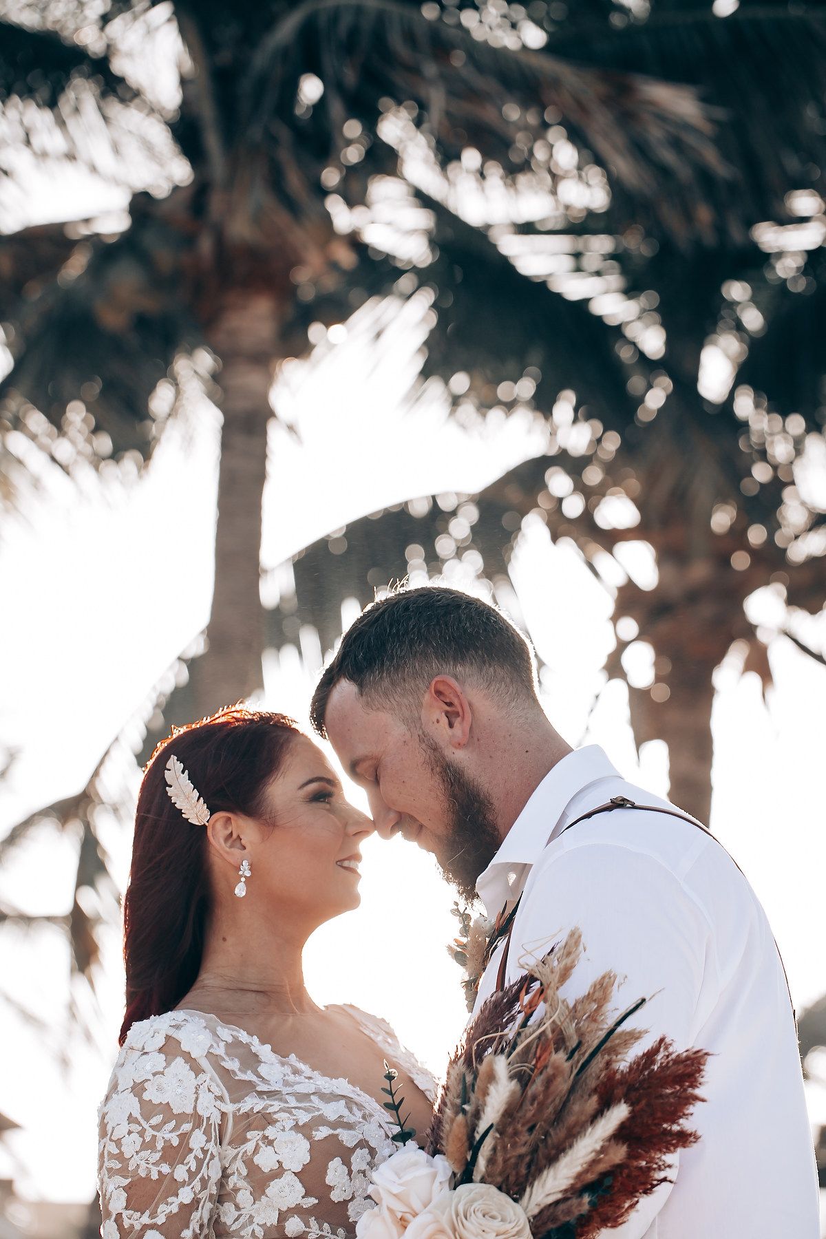 Newlyweds share romantic moments under palm trees during golden hour photo session.