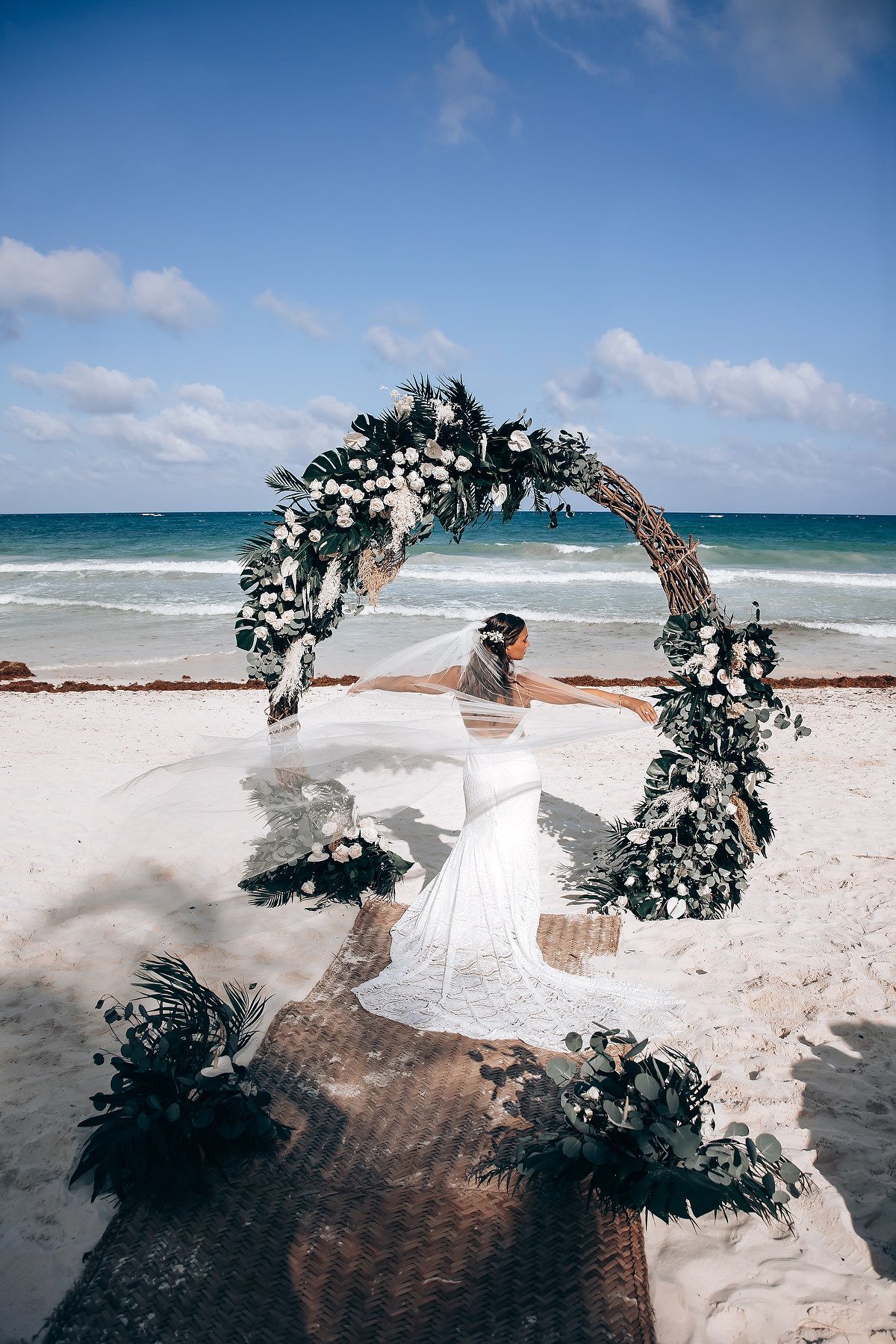 Floral arch setup on a white sandy beach with turquoise ocean waters and blue sky in the background.